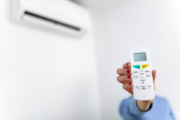 Woman holding a remote of a modern airconditioner unit at home.