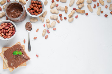 Jar of chocolate paste. Decorated with peanuts and hazelnuts. Next to a can of toast and a spoon..Flat lay composition. View from above. White background. Space for text.