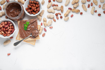 Jar of chocolate paste. Decorated with peanuts and hazelnuts. Next to a can of toast and a spoon..Flat lay composition. View from above. White background. Space for text.