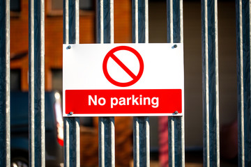 Close up view of a red & white No Parking sign attached to a metal security fence, at an industrial trading estate in Colliers Wood, London, UK.