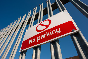 Low angle view, of a red & white No Parking sign attached to a metal security fence, at an industrial trading estate in Colliers Wood, London, UK