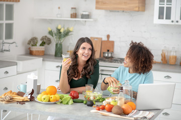 Two girlfriends preparing vegetarian food and communicate.
