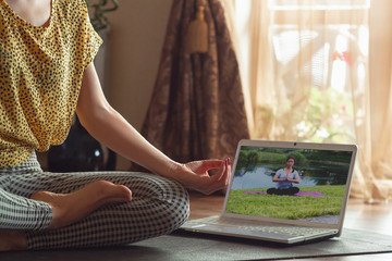Sporty young woman taking yoga lessons online and practice at home while being quarantine. Concept...