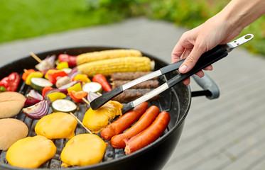 cooking, barbecue and food concept - close up of shish kebab meat, vegetables on bamboo skewers, burger buns with corn and sausages roasting on brazier grill outdoors