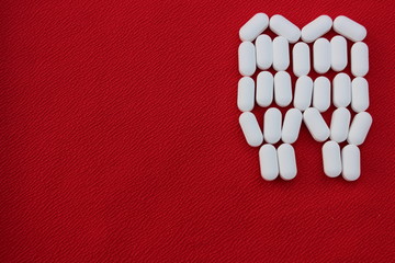 Tooth from pills on a red background. Dental clinic concept. Calcium vitamin in the form of a tooth...