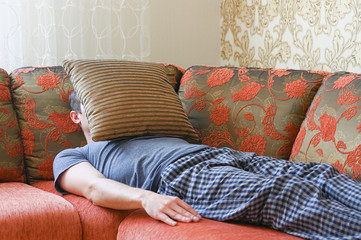 Man is lying on the couch in depression. lying on the sofa covered with a pillow.