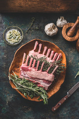 Raw lamb racks in wooden bowl with herbs and spices on rustic kitchen table , top view. Meat...