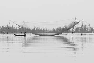 Black & White image of a traditional Fisherman under his nets on the Thu Bon river, Hoi An, Vietnam at dawn.