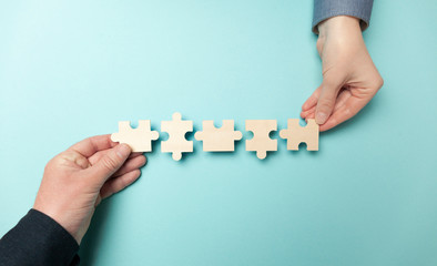 Two hands connect puzzles on a blue background. Cooperation and teamwork in business. Collaboration...