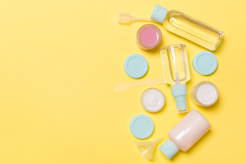 Top view composition of small travelling bottles and jars for cosmetic products on yellow background. Facial skin care concept with copy space for your design