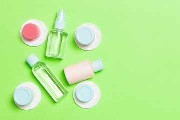 Top view of means for face care: bottles and jars of tonic, micellar cleansing water, cream, cotton pads on green background. Bodycare concept with empty cpace for your ideas