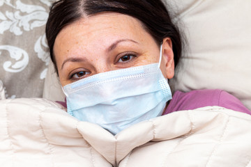 sick woman suffers with viral flu in bed in a medical mask