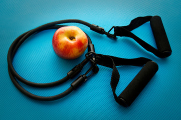 Sport expander and an apple on blue yoga mat background. Fitness gym