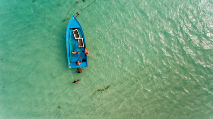 Children jumping into the water in Small fishing boat moored in blue clean transparent water. Aerial view.