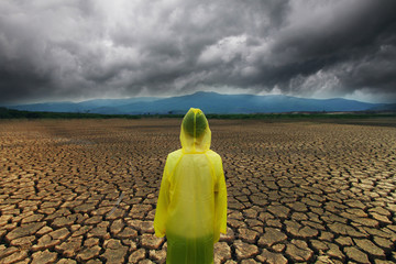Young man wear a raincoat standing on midle dry lake with storm cloud metaphor climate change and...