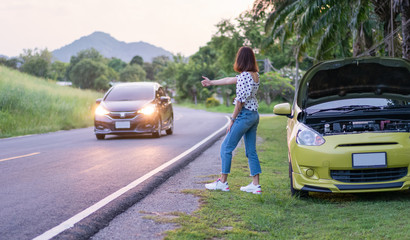 Asian young woman with broken car showing hitchhiking on the roadside. Problems with cars on the road. Road trip concept