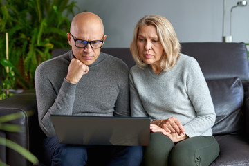 Middle-aged mom rest in living room with adult child use computer family weekend together.