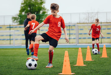 Obraz premium Boy in children's soccer team on training. Kids practicing outdoor with a soccer balls. Training football session for children on soccer camp. Young boy improving dribbling skills. Training with cones