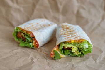 Closeup of tortilla with fried chicken meat and vegetables on sheet of paper