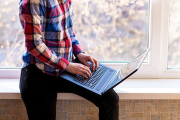 Business woman working on a laptop while sitting on a windowsill.