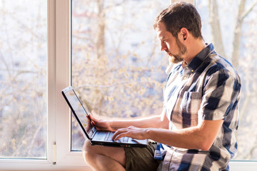 Fototapeta premium Business man working on a laptop while sitting on a windowsill.