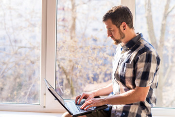 Fototapeta premium Business man working on a laptop while sitting on a windowsill.