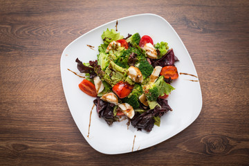 Vegetable salad with mozzarella, tomatoes, broccoli and basil in a plate on a wooden background Top view.
