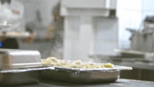 chef opens container pot with hot cooked boiled dumplings in steam lrrl. in catering canteen cafe restaurant. concept business, preparation, traditional meal. dough gedza geza vareniks