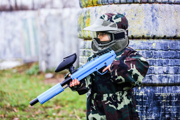 Child paintball player in camouflage standing with gun before playing outdoors