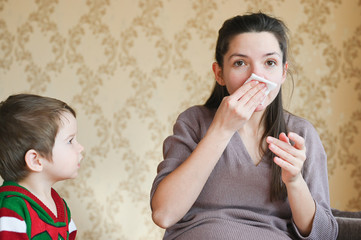Sick pregnant woman with a runny nose at home. The youngest child is looking at a pregnant mother.