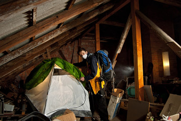 The man went on a trip to the attic. The concept of quarantine, self-isolation, pandemics and epidemic protection. Many old things in the background. Hiking at home. The tourist lays out the tent.