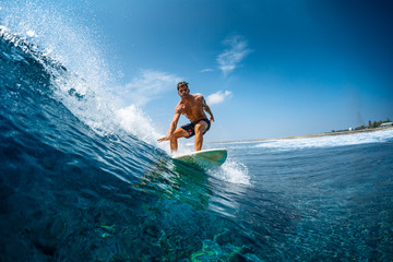 Young athletic surfer rides the wave in tropics with splashes. Jailbreaks surf spot in Maldives