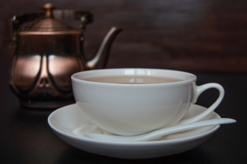 White tea cup with saucer and tea spoon on dark background.