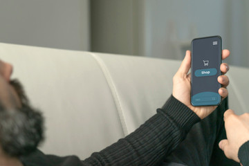 A bearded man use the smartphone for shopping online on the sofa at home