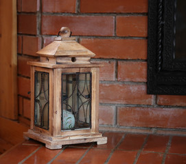 Wooden stylized antique lantern stands near the fireplace, country interior design.