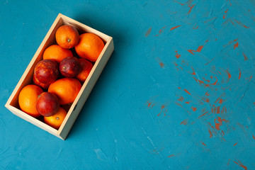 Bloody oranges in wooden box on blue concrete background top view with space. 