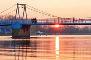 A suspension footbridge with motion blurred people silhouettes at the sunrise