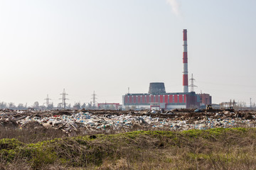 Fototapeta na wymiar A building of a thermal power station with a smoking chimney and a rubbish dump on the foreground. Concept of destroy of the earth ecosystem by human impact
