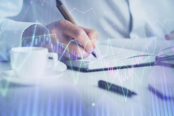 Double exposure of man's hands writing notes of stock market with forex chart.