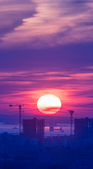 Tower cranes, the construction of a new tall apartment building at a construction site in the city at sunset or sunrise. Profitable investments and renovation program, development, verical shot