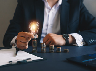 Hand businessman holding a light bulb with coins stack. Successful businessman. Creative ideas for saving money concept. Concept inspiration and innovation.