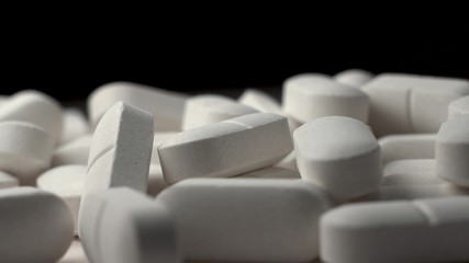 Many white pills rotate. Beautiful macro footage. The invention of tablets from coronovirus. Black background.
