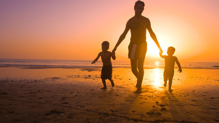 Father with kids playing in the beach at sunset