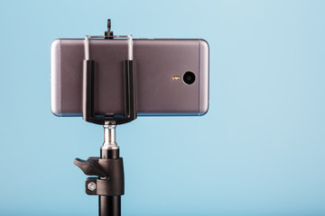 The smartphone is mounted on a tripod as a photo-video camera for a blog on a blue background. Record videos and photos.