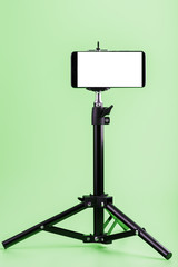 Mobile phone on a tripod with a clear white display for images and text, green isolated background.