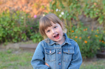 Funny little caucasian girl in denim jacket on a walk on a sunny autumn day outdoor lifestyle. The child in emotions smiling and is happy