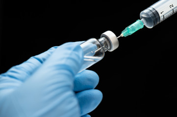 Doctor's hand holding medicine bottle and syringe isolated on black background.Nurse using syringe...