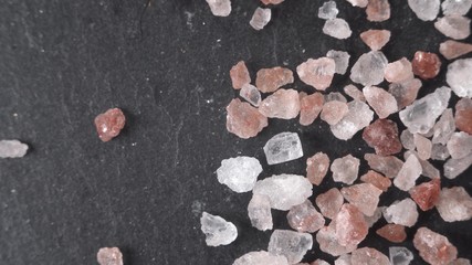 Fototapeta premium Beautiful macro shot footage close up Himalayan salt lies on a black stone. Crystals of various breeds, pink, white - lie on a fossil.