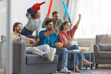 Full length portrait of multi-ethnic group of friends watching sports match on TV and cheering...