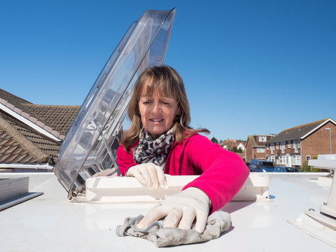 A lady motorhome owner cleans the roof of her recreational vehicle.The top half of her body is visible as she has climbed through the roof skylight.Vivid pink fleece.Amusing.Image
